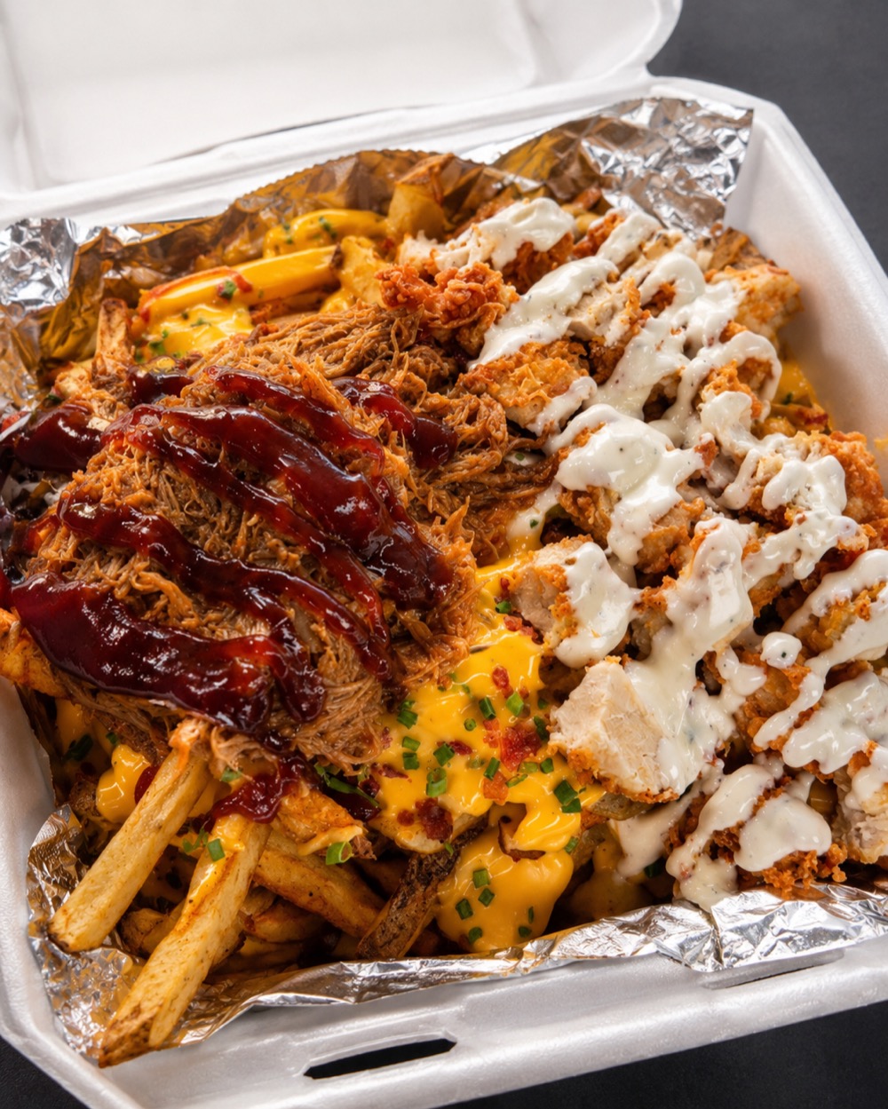 The Collision &mdash; fresh-cut fries loaded with cheese sauce, BBQ pulled pork and crispy chick'n, drizzled with ranch, in a takeout box.