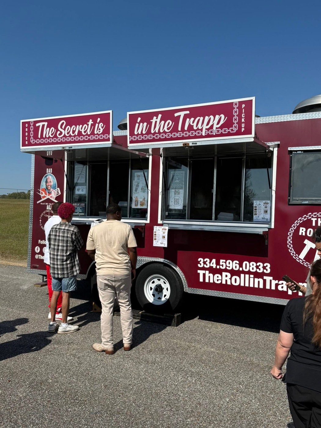 Customers ordering at The Rollin' Trapp service window, beneath signs reading The Secret is in the Trapp.