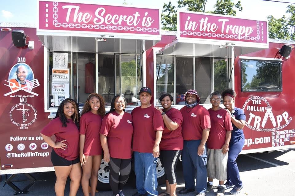 The Rollin' Trapp team of eight in matching burgundy shirts, standing together in front of the food trailer.